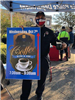 A police officer holds a cup of coffee and a sign advertising the Coffee with a Cop event