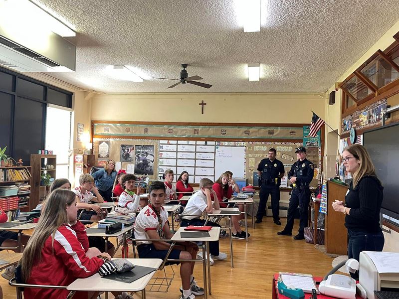 A woman and two uniformed police officers speak to a classroom of teenagers