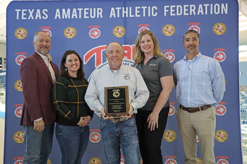 Five people stand in front of a TAAF backdrop. The man in the middle holds a plaque.
