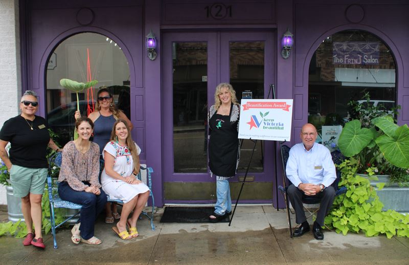 Group photo with some standing and some sitting outside a purple building with metal tubs of plants
