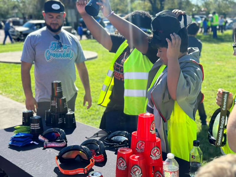 Teens wearing safety vests try to stack cups while wearing impairment goggles.