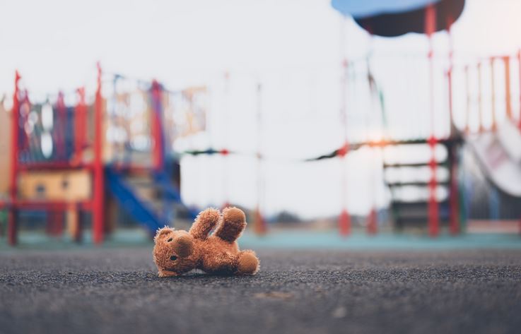 A playground with a small teddy bear lying on the ground on a cloudy day