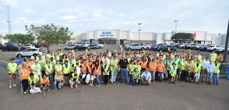 Large group of people in a Ross parking lot wearing safety vests and holding trash bags and grabbers