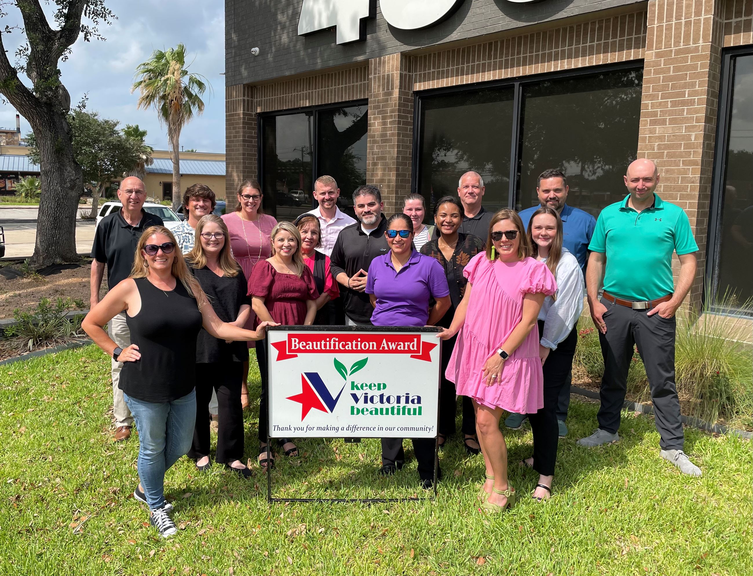 Large group photo with KVB sign on the lawn in front of a building