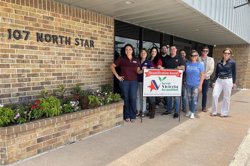 Group photo with KVB sign in front of brick building with a colorful flowerbed along the wall