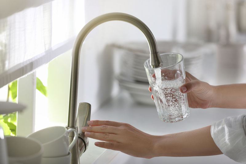 Hand filling a glass of water from a kitchen faucet