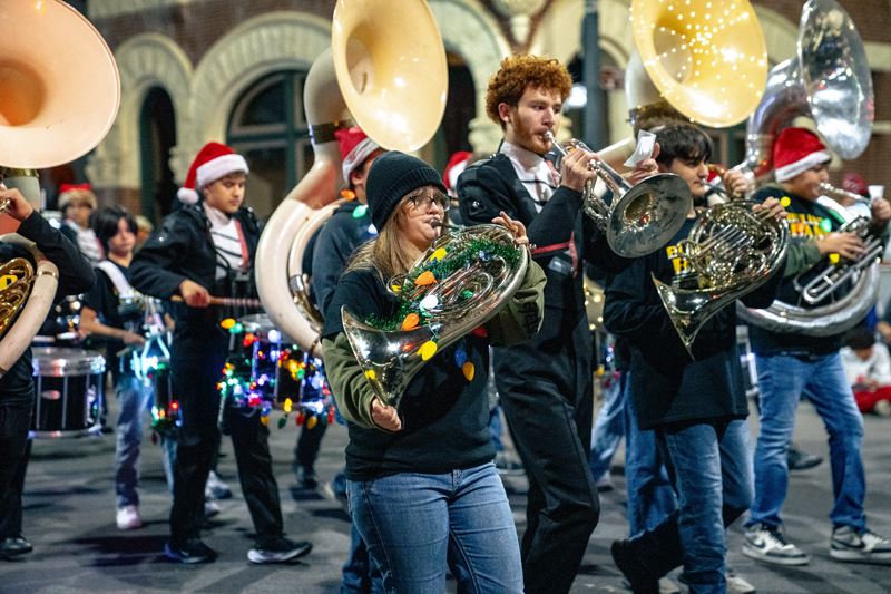 A high school marching band in a parade. Instruments decorated with Christmas lights and tinsel.
