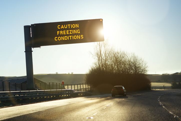 A highway with a light-up sign overhead reading Caution, Freezing Temperatures