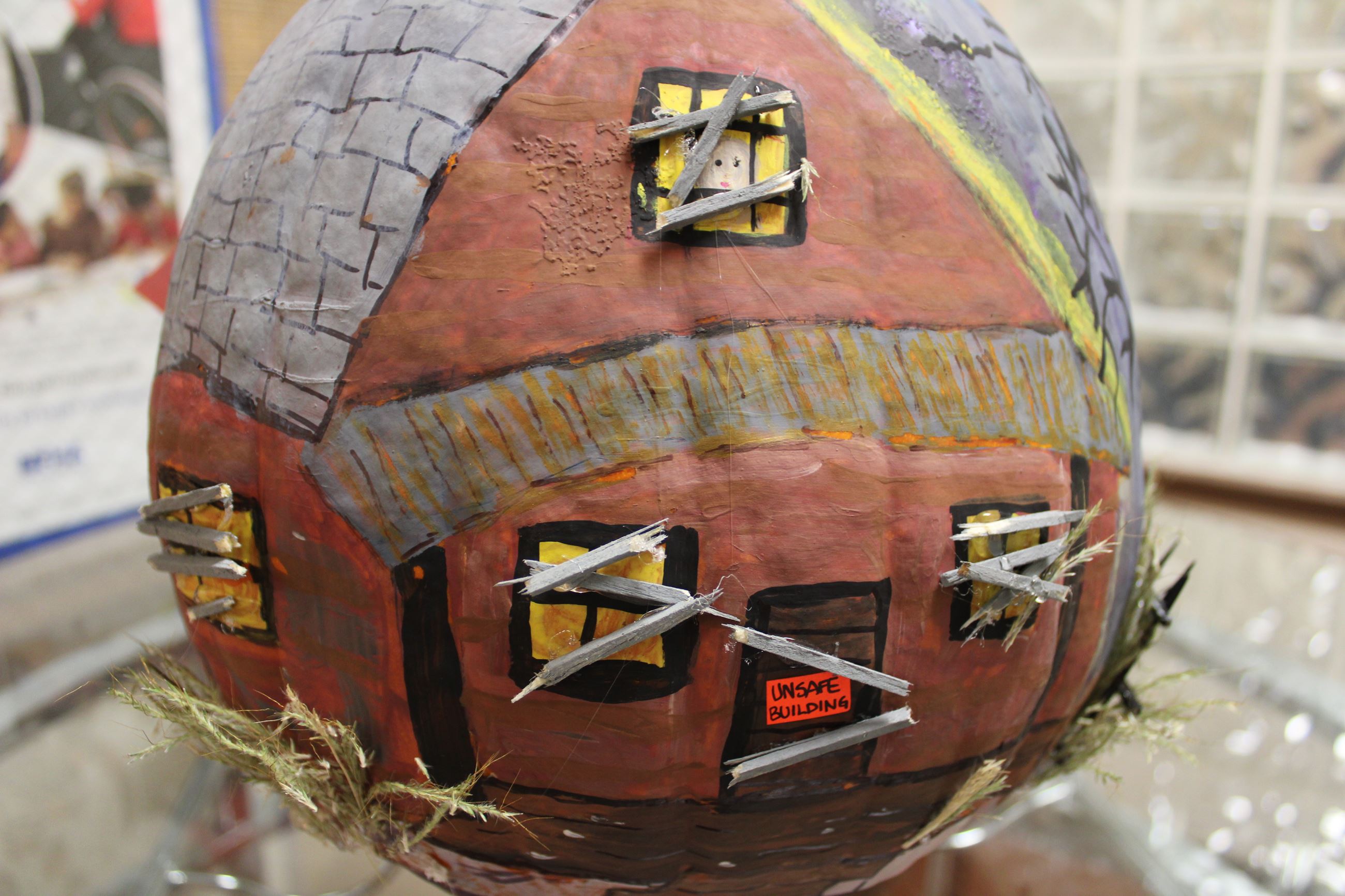 Pumpkin painted as eerie house with boarded windows. An orange notice is on the door.