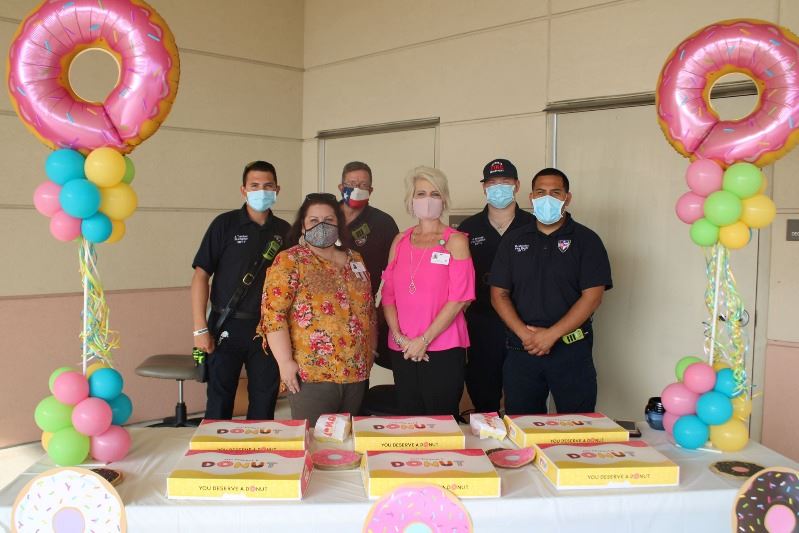 Six people, four in firefighter polos, pose with table full of donut boxes and donut-shaped balloons