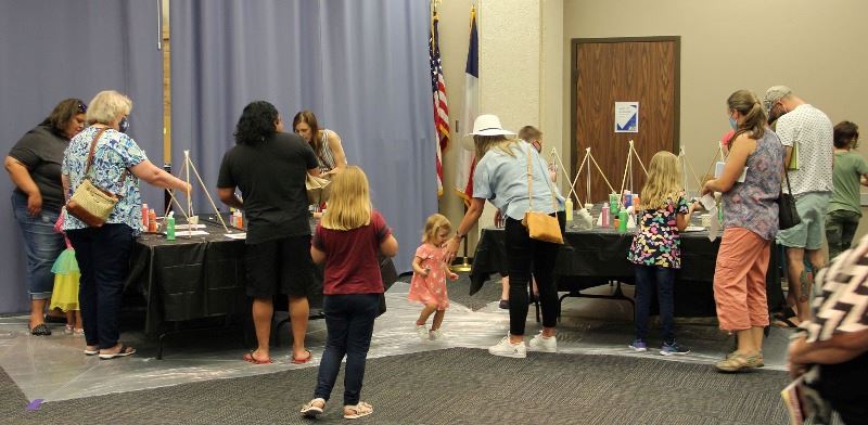 People of different ages gather around tables in the Bronte Room with paint and craft activities.