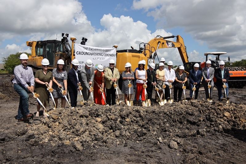 Group of people in hard hats dig ceremonial shovels into a pile of dirt