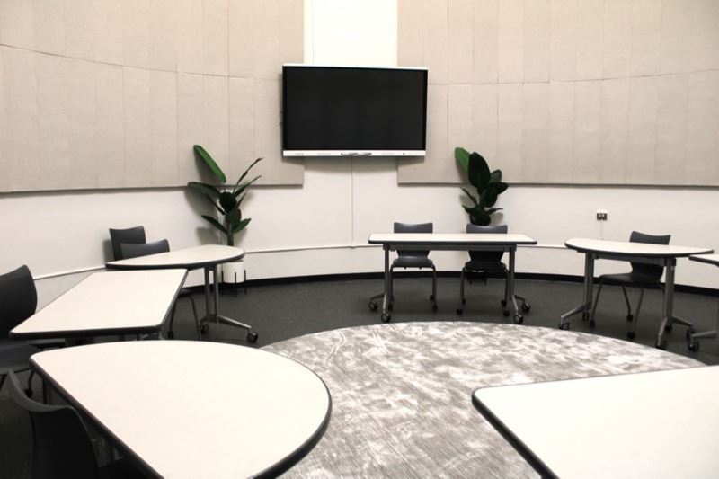 Meeting tables arranged in a circle with a 75-inch monitor in the background.