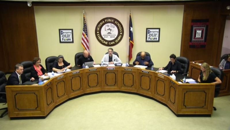 People seated around school board dais with VISD logo on back wall.