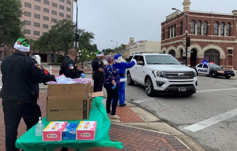 Blue anta and others in uniforms or Christmas attire stand on DeLeon Plaza sidewalk.