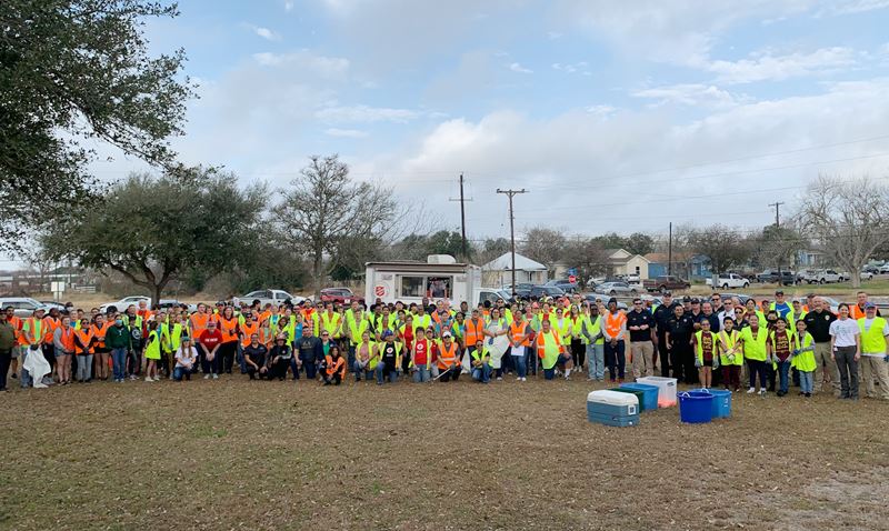 Group photo of more than 100 people wearing safety vests in a park.