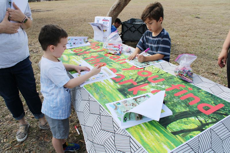 Young kids use markers to fill out colorful forms at a table outside