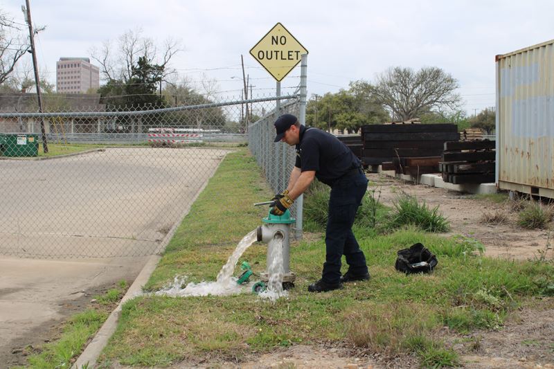 A man in a cap lets water flow from the side spouts on a fire hydrant