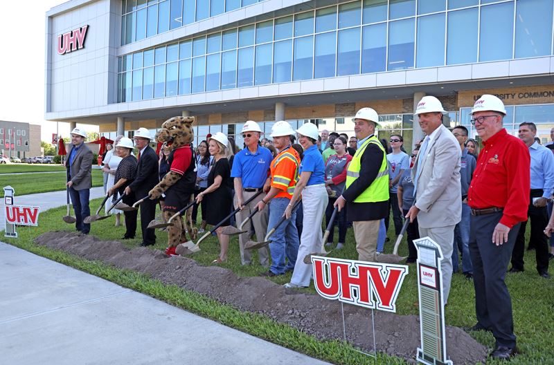 Group photo in front of UHV building with people in foreground digging shovels into dirt.