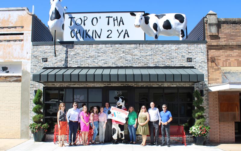 Group photo with Chick fil A cow and several people at a building with Chick fil A cows on the roof