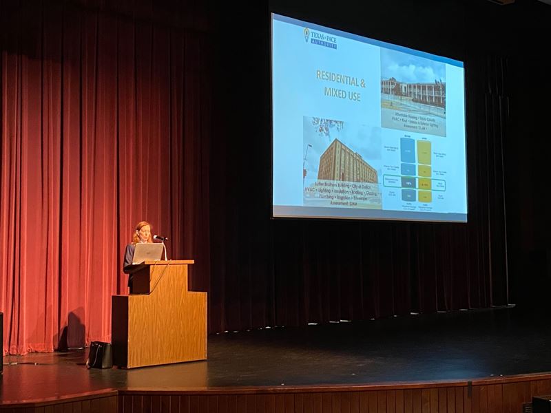 A woman stands at a podium with a projector screen behind her with information about Texas PACE