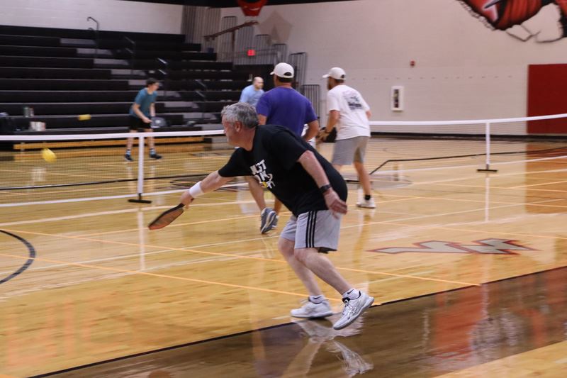 A pickleball player goes for a shot in a pickleball court set up in an indoor basketball court.