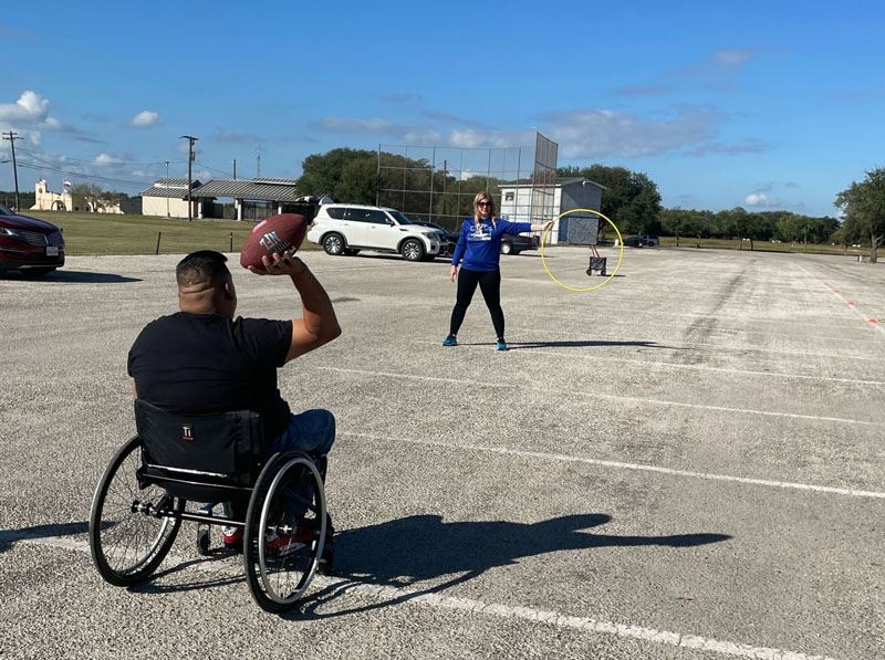 A man in a wheelchair raises a football to throw through a hula hoop held by a woman.