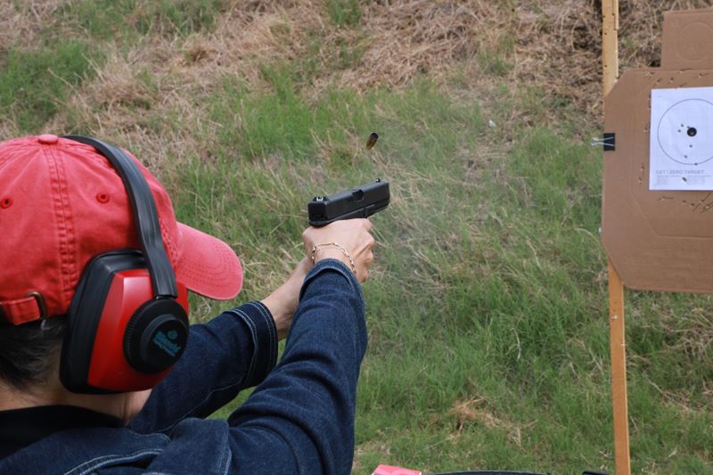 A person wearing a hat and ear-protecting headphones fires a handgun at a target