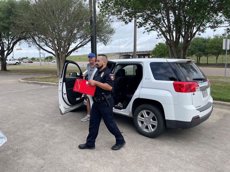 Uniformed police officer carrying a small red crate away from a white hatchback