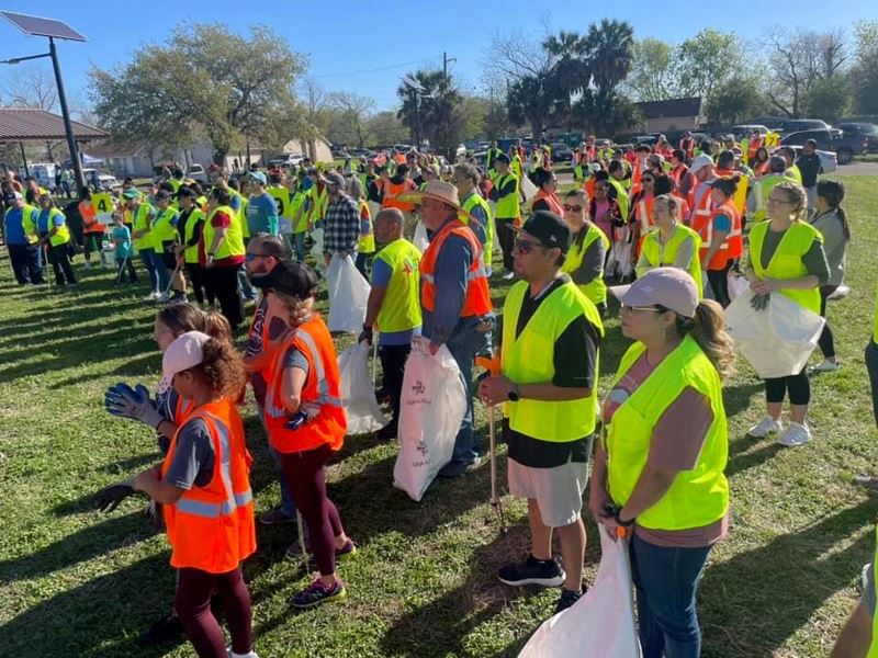 People in orange and yellow work vests holding trash bags in a park