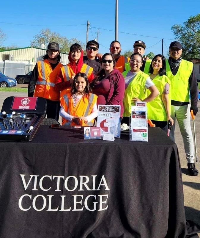 People in orange and yellow work vests stand at an outdoor table with a Victoria College tablecloth