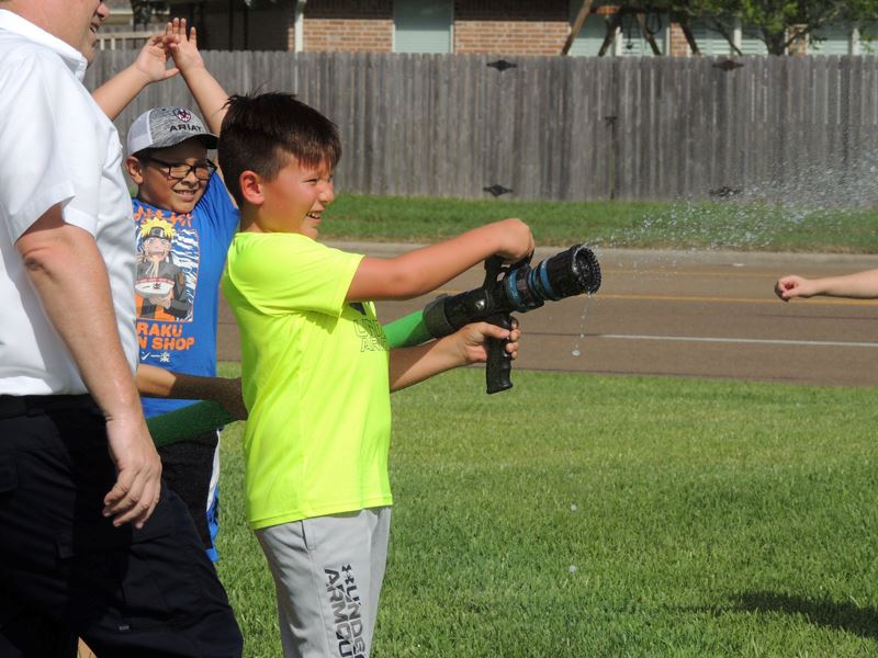 A smiling boy aims a fire hose