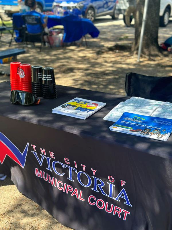 A table outdoors with a Municipal Court tablecloth, flyers, impairment goggles and stacking cups