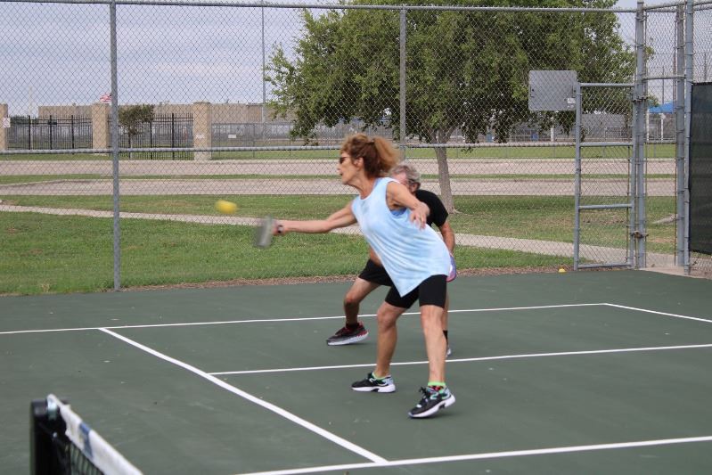 A woman playing pickleball reaches to hit the ball.