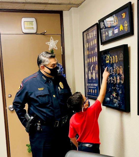 Boy points to a badge in a framed badge display while police chief looks on.