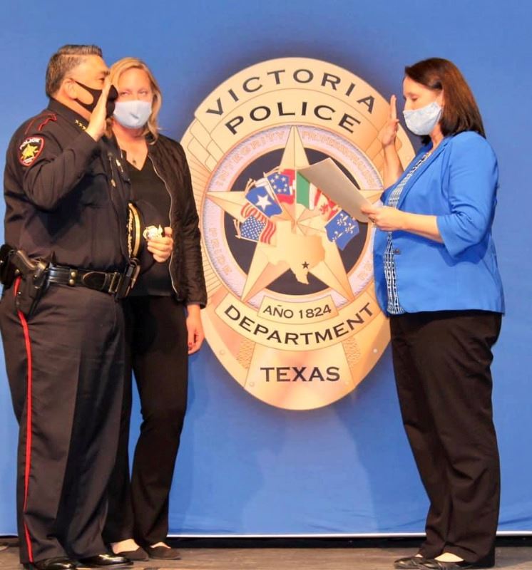 Uniformed police chief onstage with woman next to him raises hand to be sworn in by city secretary.
