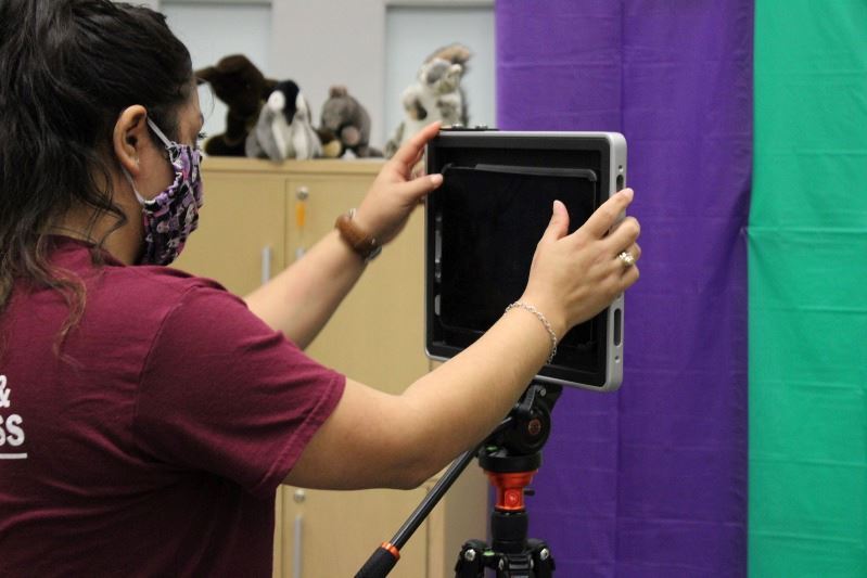 A woman sets up an iPad on a tripod to film a colorful fabric backdrop.