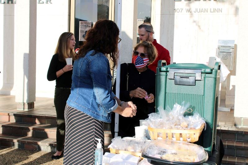 A few people stand near a refreshments table under a canopy in front of the Municipal Court building