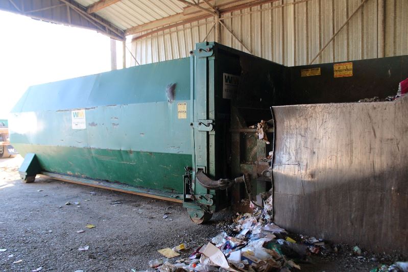 A green compacting machine that looks like a shipping container sits in a warehouse.