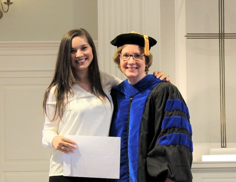 Smiling woman holds certificate next to older woman in academic regalia