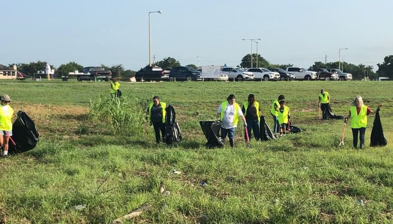 People in yellow safety vests pick up trash in a grassy field