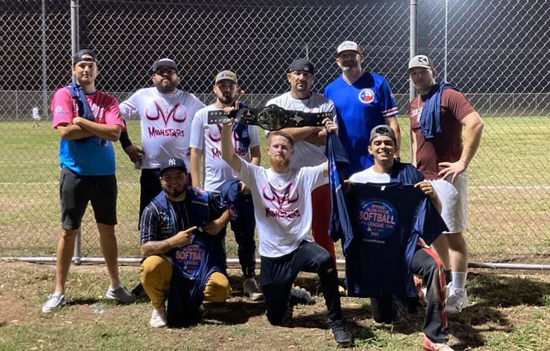 Group photo outside softball field. One player holds a championship belt.