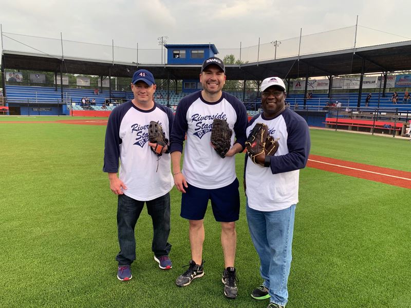 Three people wearing Riverside Stadium shirts and holding ball gloves