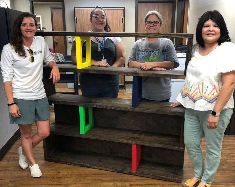 Four people pose for a photo with a bookshelf