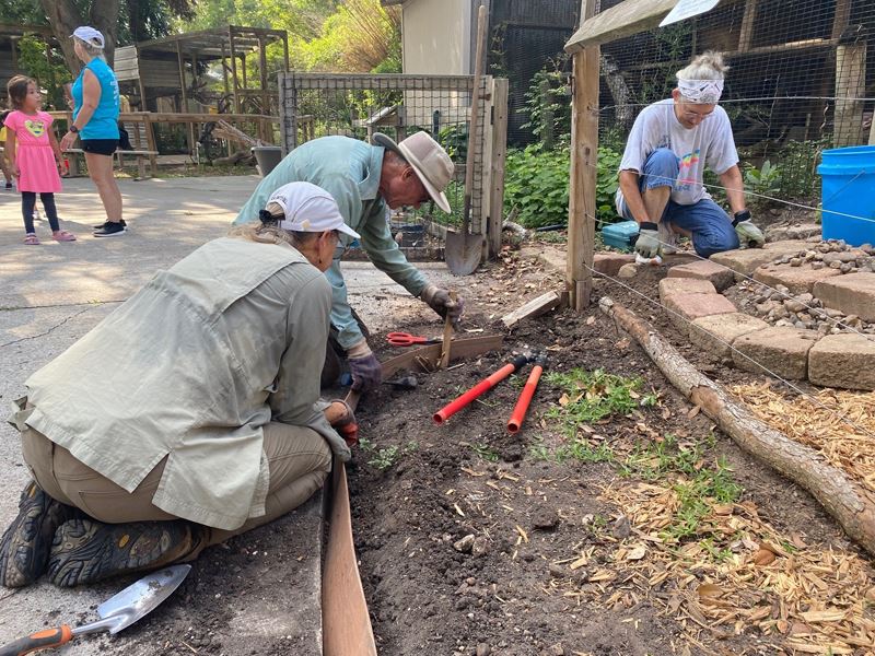 Three people arrange stones and bordering in flowerbeds