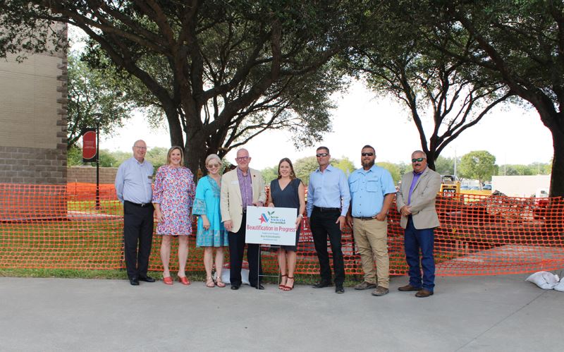 Group photo at an area with grass and overturned dirt blocked by orange mesh. UHV logo on flag.